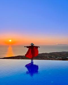 una persona con una capa parada en una piscina viendo la puesta de sol en Luna Rossa en Imerovigli