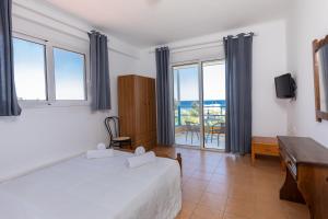 een slaapkamer met een bed, een bureau en ramen bij Plastiras Sea View Apartments in Archangelos