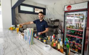 a man standing behind a counter with a drink at Epicentrum Suites Fresh in Limenaria