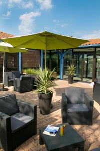a patio with chairs and tables and an umbrella at Kyriad Prestige - Bordeaux Aeroport in Mérignac