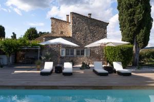 un patio avec des chaises et des parasols à côté d'une piscine dans l'établissement La Bastide des Cyprès - L'ESCAPADE ADULT ONLY, à Les Mées