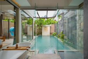 an indoor pool in a house with a bathtub and glass walls at Lalasa Villas Canggu in Canggu