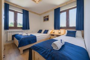 two beds in a room with blue curtains and windows at Wierchowe Apartamenty in Leśnica
