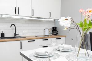 a kitchen with white cabinets and a table with glasses and flowers at Lux Apartament z Widokiem na MORZE - Mazowiecka 213 by Renters in Pobierowo