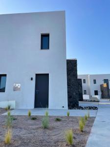 un edificio blanco con una puerta negra y algunas plantas en myLithos Suites en Monolithos