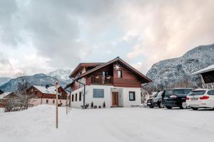 een huis in de sneeuw met auto's geparkeerd bij Bergmoment Apartments in Obertraun