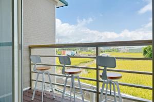 d'un balcon avec trois tabourets et vue sur un champ. dans l'établissement 喫茶居 茶蔬食主題民宿 Chih Cha Jyu, à Gongguan