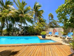 a swimming pool with a wooden deck and palm trees at Caraiba Villa & Bungalows in Sainte-Anne