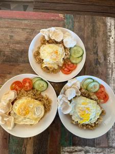 three plates of food with eggs and tomatoes on a table at Cabana Surf and Stay in Biha