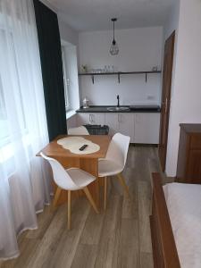 a small kitchen with a wooden table and white chairs at POKOJE GOŚCINNE DOMINIK in Ostrowo