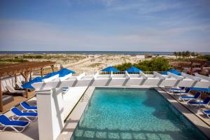 a swimming pool with chairs and blue umbrellas at Mahalo Diamond Beach Resort in Wildwood Crest