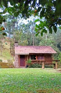 uma cabana de madeira com um telhado vermelho num campo em Chalé do Coiote em Maromba em Visconde de Mauá