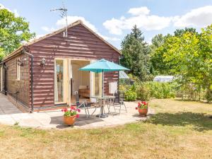 ein kleines Holzhaus mit einem Tisch und einem Sonnenschirm in der Unterkunft Norbank Garden Studio in Bressingham