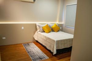 a small bedroom with a bed with yellow pillows at Apartamentos Studio no centro de Foz do Iguaçu in Foz do Iguaçu