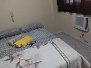Un dormitorio con una cama con una maleta amarilla. en STUDIO Centro Lacerda, en Campos dos Goytacazes