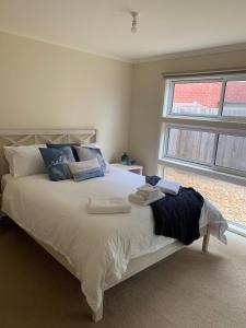 Un dormitorio con una cama blanca con almohadas azules y una ventana en Contemporary On Cuttriss - Inlet Side, en Inverloch