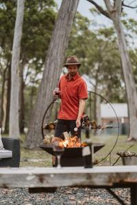 a man standing next to a grill with fire at Bay and Bush Cottages Jervis Bay in Huskisson