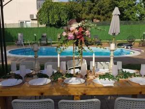 drewniany stół z kwiatami i świecami przed basenem w obiekcie Vila Mila Riverside Apartments w mieście Smederevo