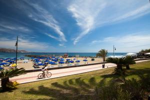 a beach with blue umbrellas and a person riding a bike at Optimist Tenerife in Playa de las Americas