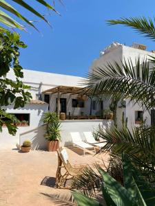 a patio with white chairs and plants in front of a building at Can Yuca II in Cala Mondrago