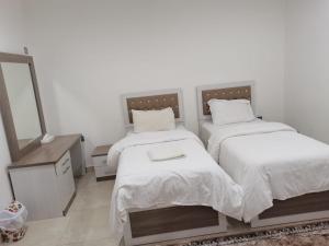 a bedroom with two beds with white sheets and a mirror at Roza Hotel Apartments in Muscat
