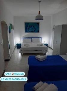 2 camas en una habitación con sábanas azules y una pintura azul en Le Volte, en Ragusa