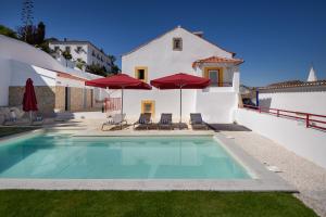 a swimming pool with chairs and umbrellas and a house at Casa Lidador - Obidos in Óbidos