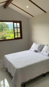 Cama blanca en habitación con ventana en Casa Aconchego I, en Pomerode