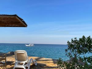 une chaise sur la plage avec un bateau dans l'eau dans l'établissement La Siesta Hotel Al Sokhna, à Ain Sokhna