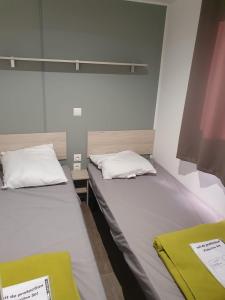 two beds in a small room with white sheets and a yellow blanket at Mobil home - Clim, TV - Camping '4 étoiles' - Narbonne Plage - 014 in Narbonne-Plage