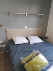 Una cama con dos almohadas y una bolsa. en Mobil home - Clim, TV - Camping '4 étoiles' - Narbonne Plage - 014, en Narbonne-Plage