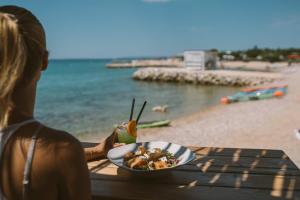 a woman sitting at a table with a bowl of food at the beach at Terra Park Phalaris in Novalja
