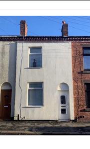 a white house with two windows and a cat in the window at Cheerful 2 bedroom house in Hindley