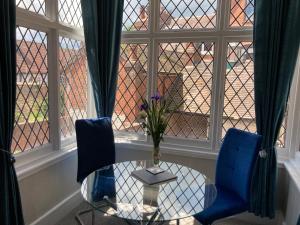 a glass table and two blue chairs in a room with a window at Rooftops - bijou sister apartment to Assembly View in Ludlow