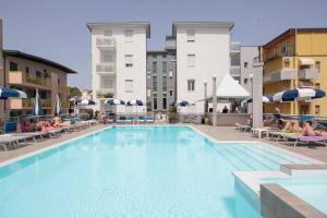 a large swimming pool with people sitting on chairs in a hotel at Hotel Bristol in Caorle