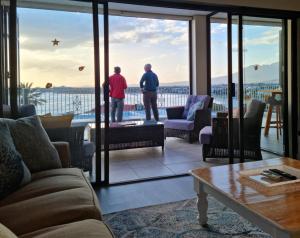 two men standing in a living room looking out at the ocean at Die Braaihuis, sleeps 6, Central and Fabulous! in Gordonʼs Bay