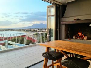 a balcony with a wooden table and a fireplace at 'Die Braaihuis'- sleeps 6, Large Veranda, Sea Views, Central and Fabulous! in Gordonʼs Bay