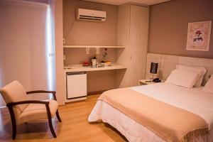 a bedroom with a bed and a chair and a kitchen at Hotel Marques in Araras