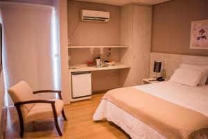 a bedroom with a bed and a chair and a kitchen at Hotel Marques in Araras