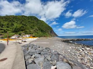 a beach with rocks and the ocean and a mountain at Casa do sanguinho in Faial da Terra