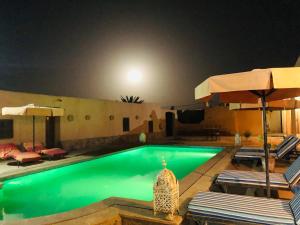 a swimming pool with chairs and umbrellas at night at Riad Hotel Les Flamants in Merzouga
