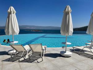 Eine Gruppe von Stühlen und Sonnenschirmen neben einem Schwimmbecken in der Unterkunft Beach front apartment in Bogazici