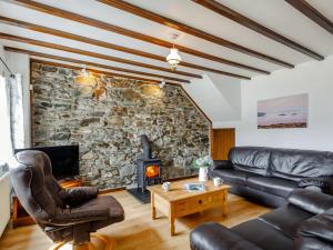 a living room with leather furniture and a stone wall at Pen Y Bont in Aberdaron