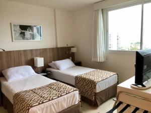 a hotel room with two beds and a television at Flat pensado para sua tranquilidade e alegria in Campos dos Goytacazes