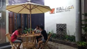 three people sitting at a table under an umbrella at Walasa Ayu Homes By MSH in Piyono
