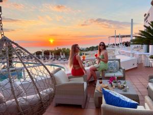 two women sitting on the roof of a hotel with drinks at Paradiso Terme Resort & SPA con 5 piscine termali in Ischia