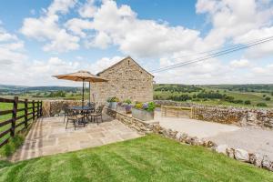 a patio with an umbrella and a table and chairs at Pogles Wood Cottage in Skipton