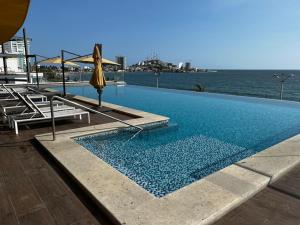 a swimming pool with an umbrella and chairs and the ocean at Luxury condo en Malecón, Alberca Infinity & Jacuzzi in Mazatlán