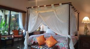 a bedroom with a canopy bed and a chair at Rambutan Hotel in Lovina