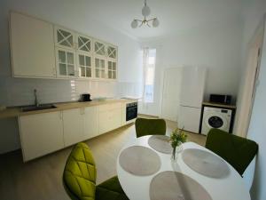 a white kitchen with a table and green chairs at Suite № 7 in Braşov +7 photos